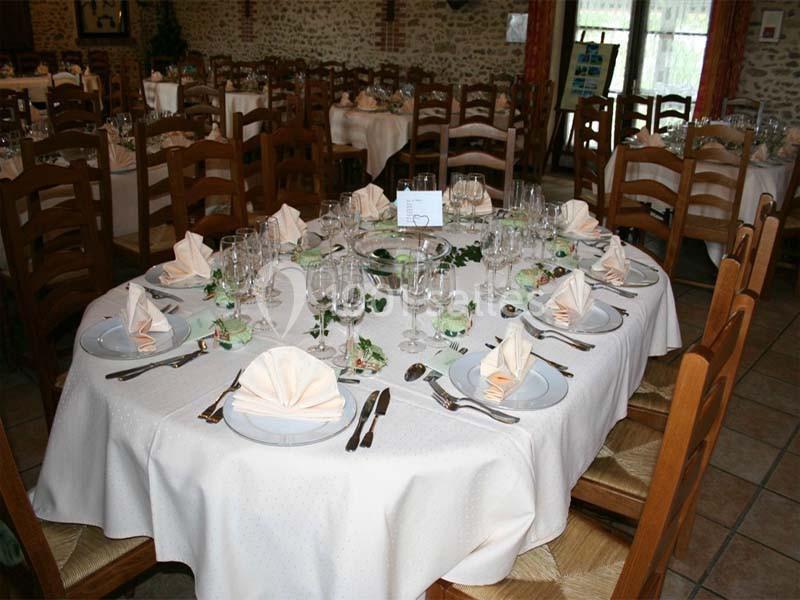 Table ronde dressée avec nappes blanches, serviettes pliées, verres et couverts dans une salle de réception rustique.