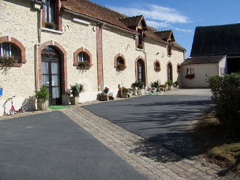 Façade d'un bâtiment en pierre avec des fenêtres en arc, des jardinières et une cour pavée.