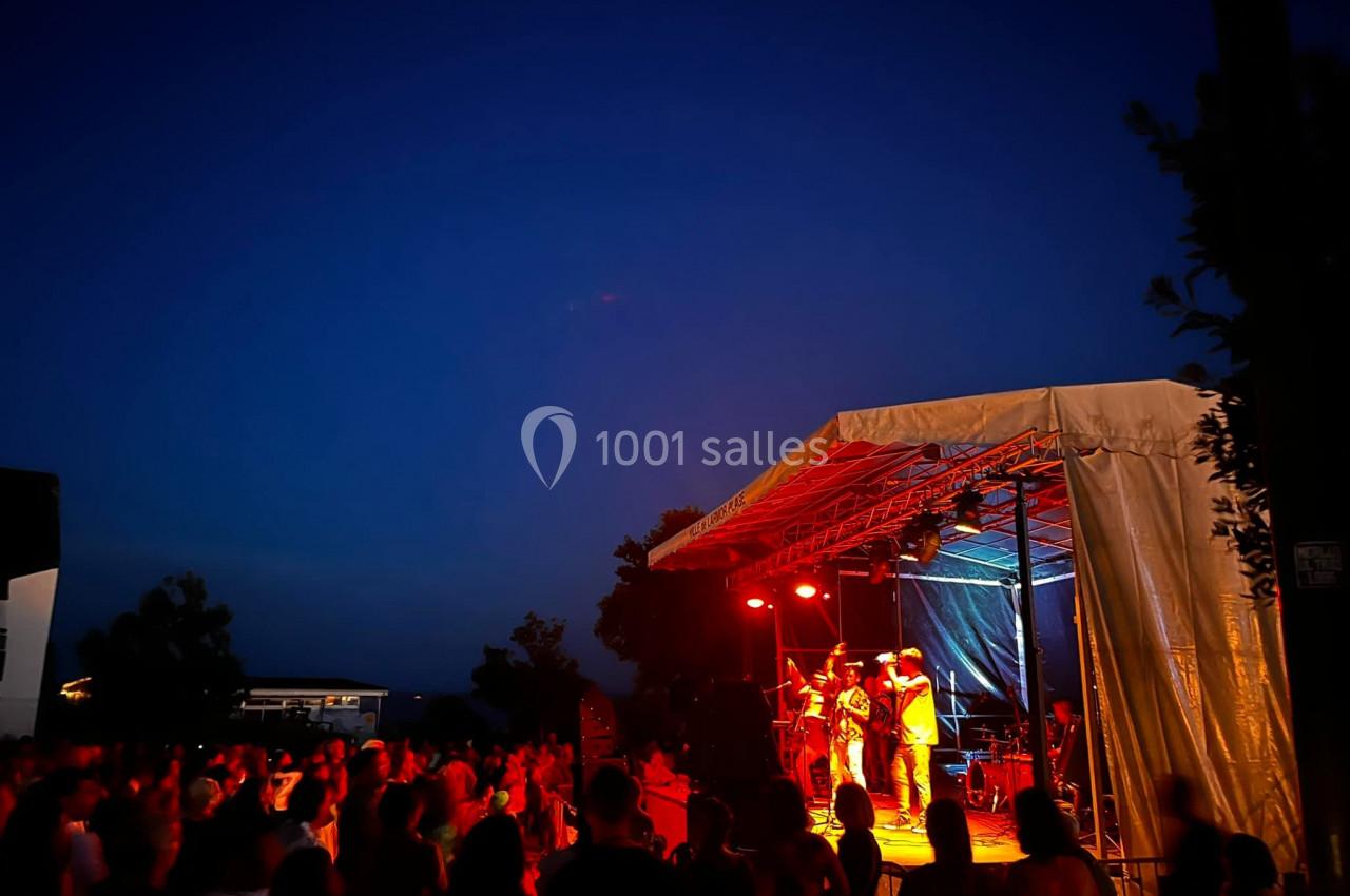 Scène extérieure éclairée en rouge avec un groupe jouant devant un public sous un ciel nocturne dégagé.