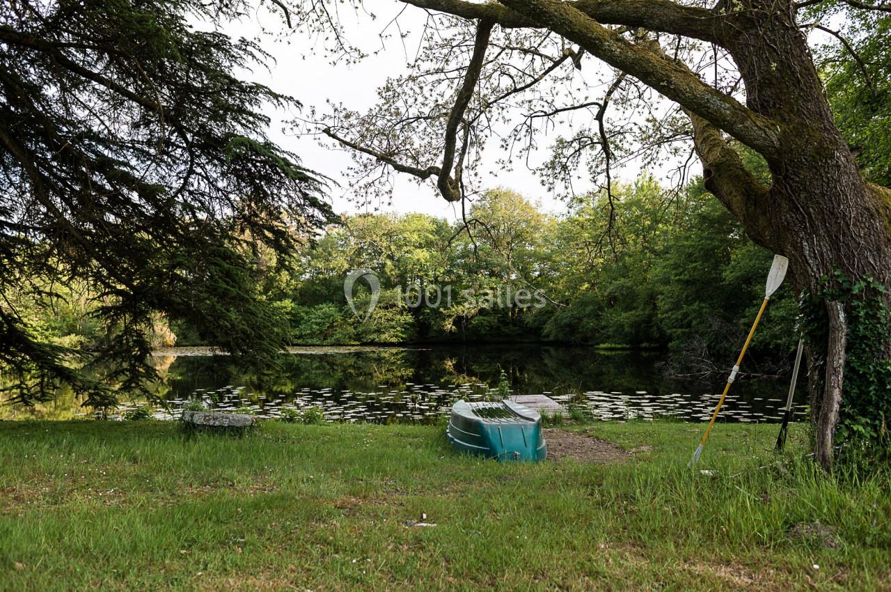 Barque verte et rame posées près d'un étang entouré d'arbres, avec nénuphars à la surface de l'eau.