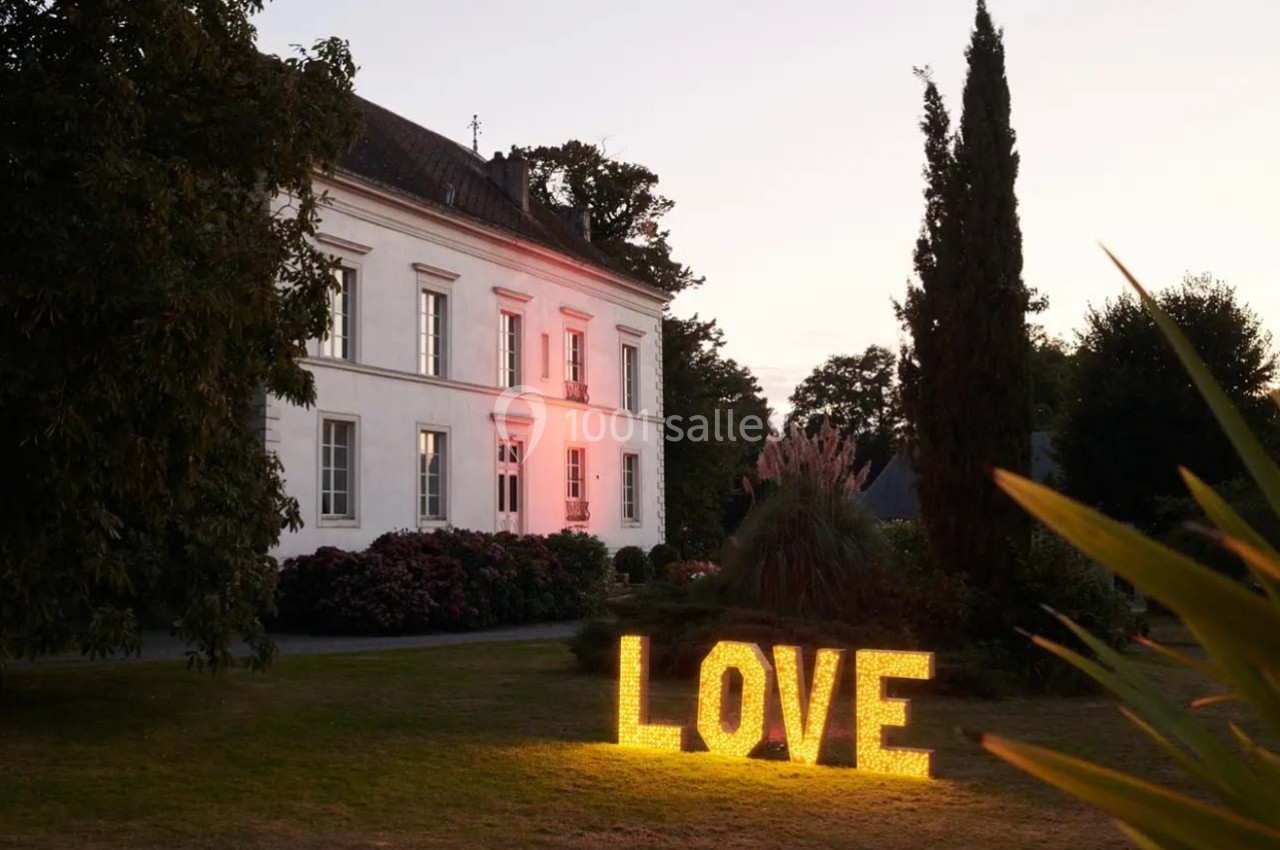 Façade d'une maison blanche au crépuscule avec le mot ’LOVE’ illuminé dans le jardin.