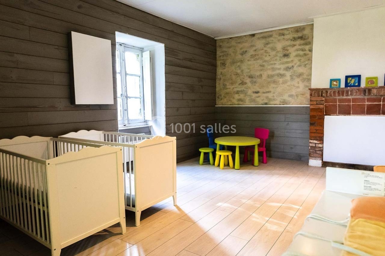 Deux lits pour enfants, une table avec des chaises colorées et un mur en pierre dans une pièce lumineuse.