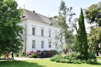 Pelouse verdoyante entourée de grands arbres sous un ciel partiellement nuageux.