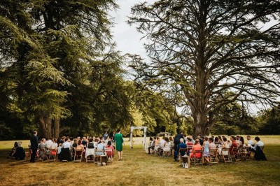 Pelouse verdoyante entourée de grands arbres sous un ciel partiellement nuageux.