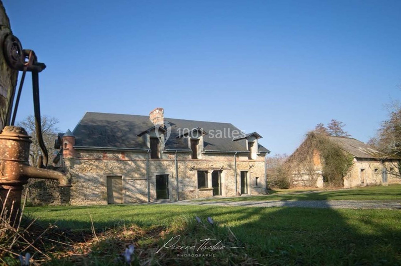 Bâtiments en pierre dans un cadre rural, entourés d'arbres et d'une pelouse, éclairés par une lumière douce.