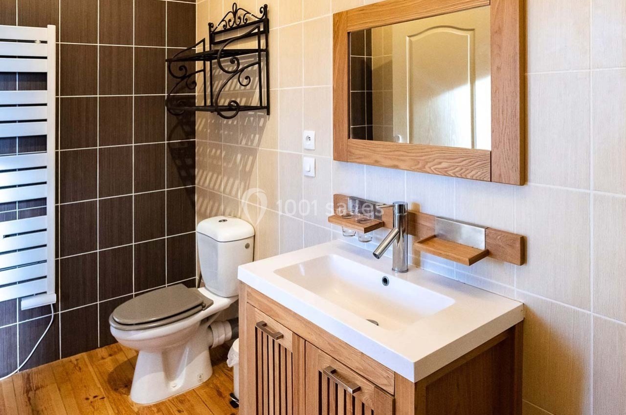 Salle de bain avec lavabo en bois, miroir assorti, toilettes blanches et mur carrelé dans des tons neutres.