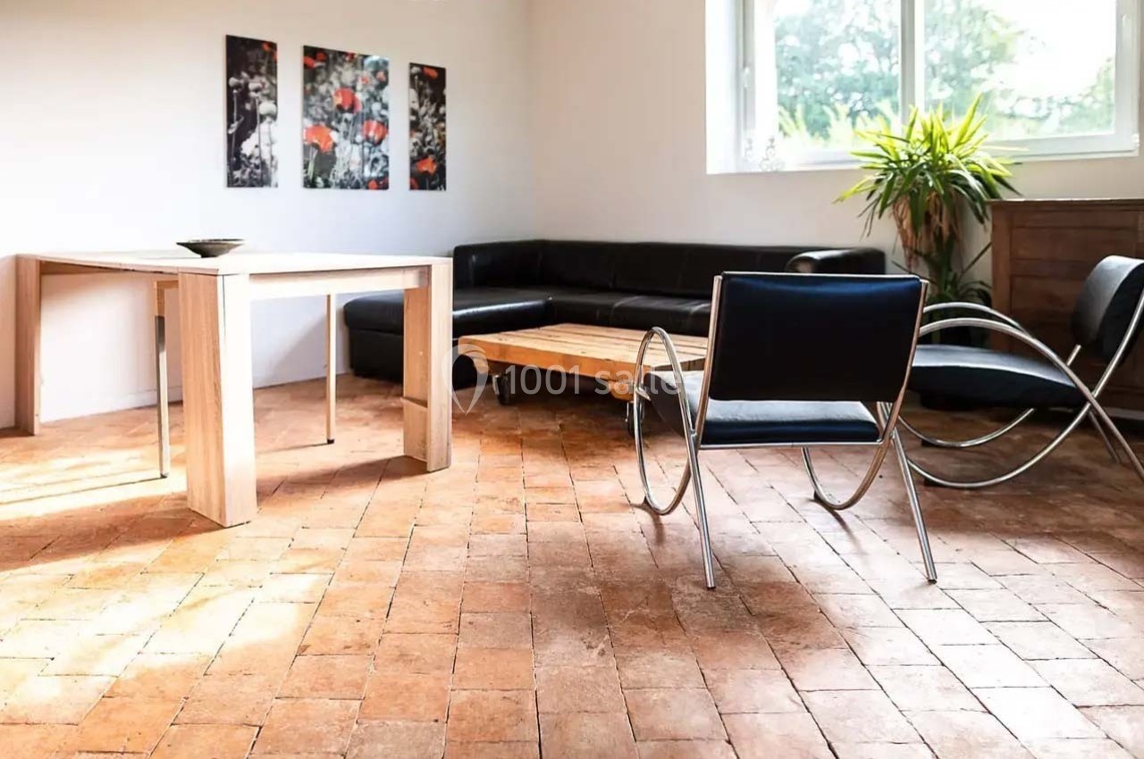 Salle de séjour lumineuse avec sol en terre cuite, mobilier moderne et plantes près d'une fenêtre.