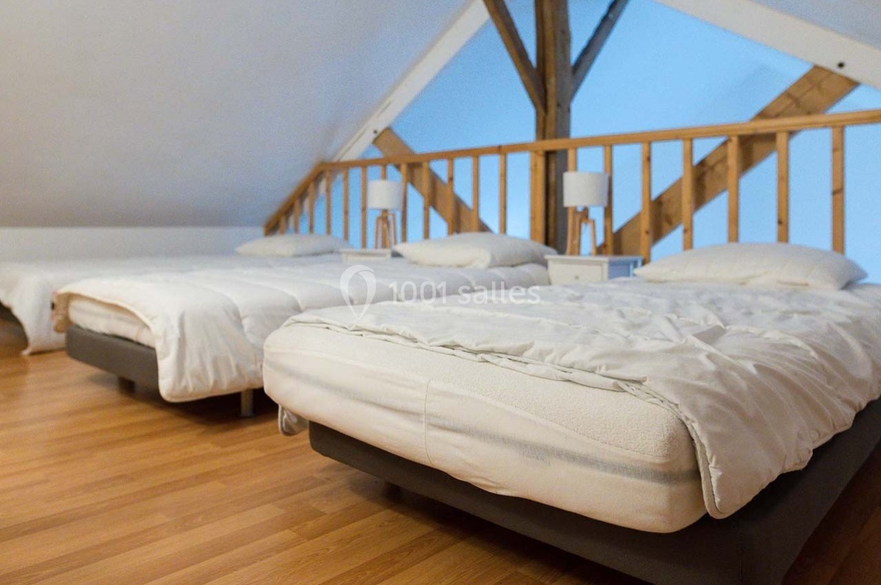 Trois lits simples alignés dans une chambre mansardée avec parquet et poutres apparentes.