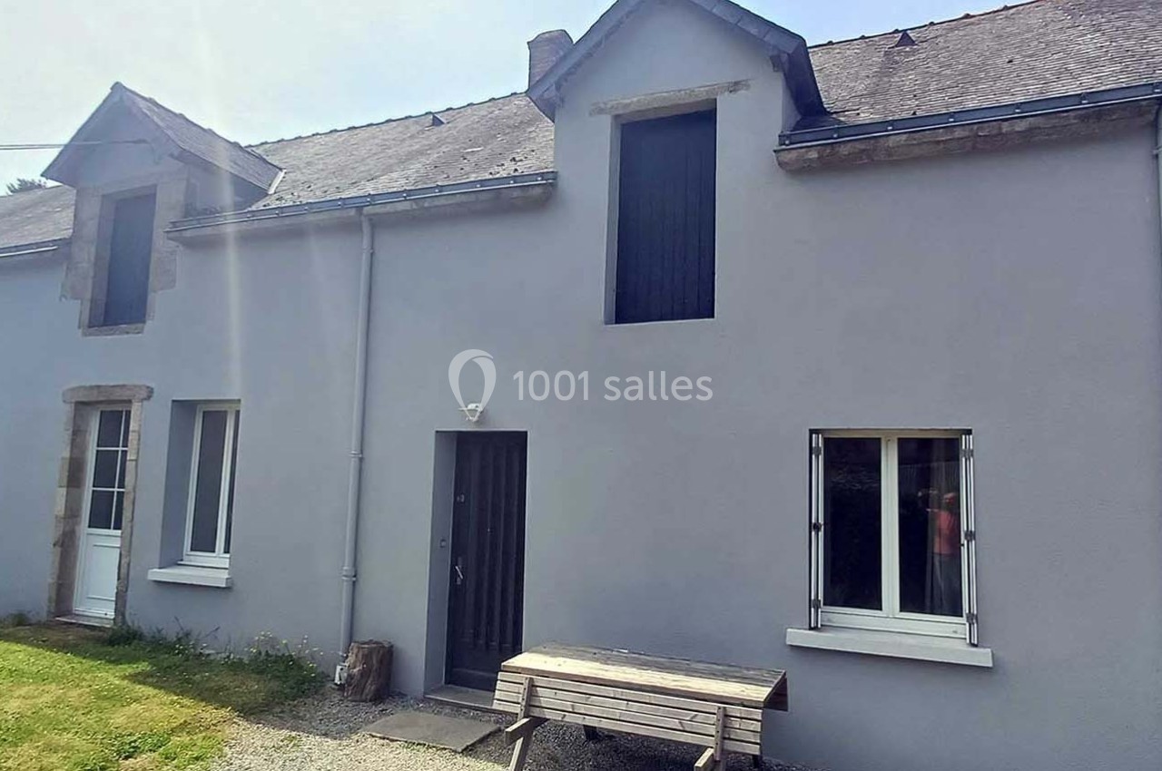 Façade d'une maison en pierre rénovée avec un enduit gris, fenêtres modernes et une table en bois devant.