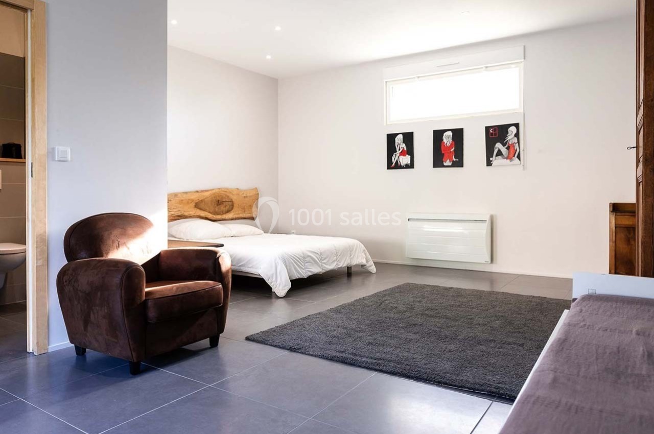 Chambre lumineuse avec lit double, fauteuil en tissu marron, tapis gris et décorations murales modernes.