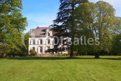 Étang calme entouré d'arbres avec un bâtiment blanc visible en arrière-plan sous un ciel bleu.