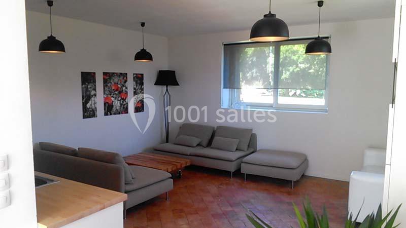 Salon moderne avec canapés gris, table basse en bois, lampes suspendues noires et fenêtre avec store.