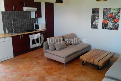 Étang calme entouré d'arbres avec un bâtiment blanc visible en arrière-plan sous un ciel bleu.