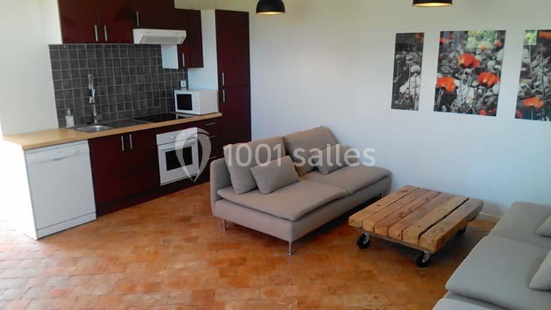 Cuisine ouverte avec meubles rouges, carrelage au sol, canapé gris, table basse en bois sur roulettes et décor mural floral.