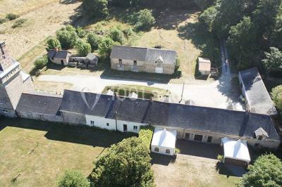 Étang calme entouré d'arbres avec un bâtiment blanc visible en arrière-plan sous un ciel bleu.