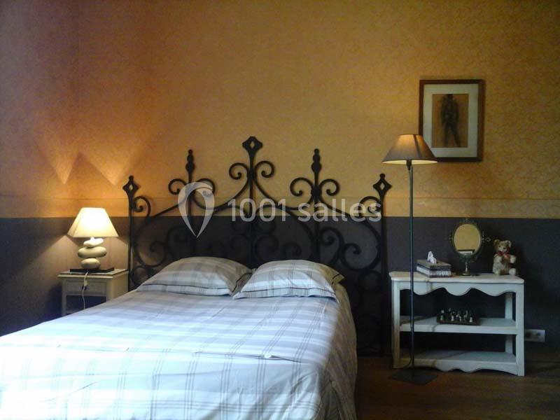 Lit double avec tête de lit en fer forgé, entouré de deux tables de chevet avec lampes, dans une chambre aux tons chauds.