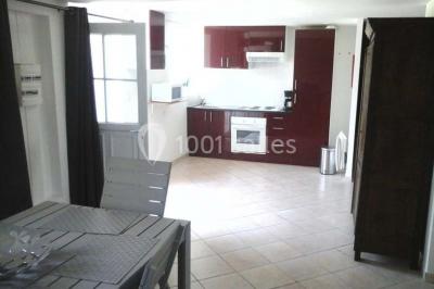 Étang calme entouré d'arbres avec un bâtiment blanc visible en arrière-plan sous un ciel bleu.