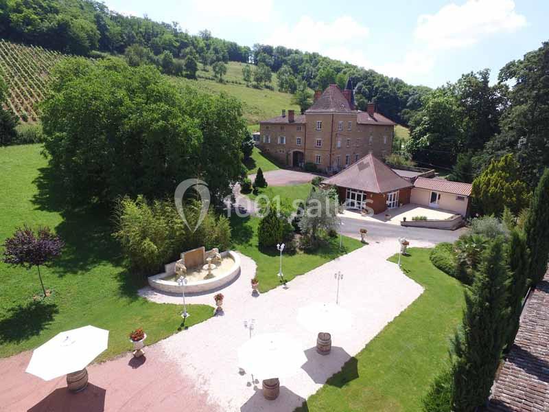 Vue aérienne d'un domaine avec une grande maison en pierre, une fontaine, des parasols et un paysage verdoyant.