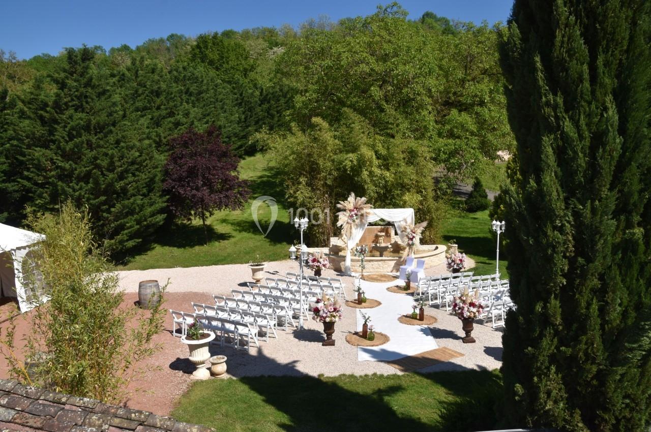 Cérémonie de mariage en plein air avec des chaises blanches disposées autour d'une arche décorée, entourée de verdure.