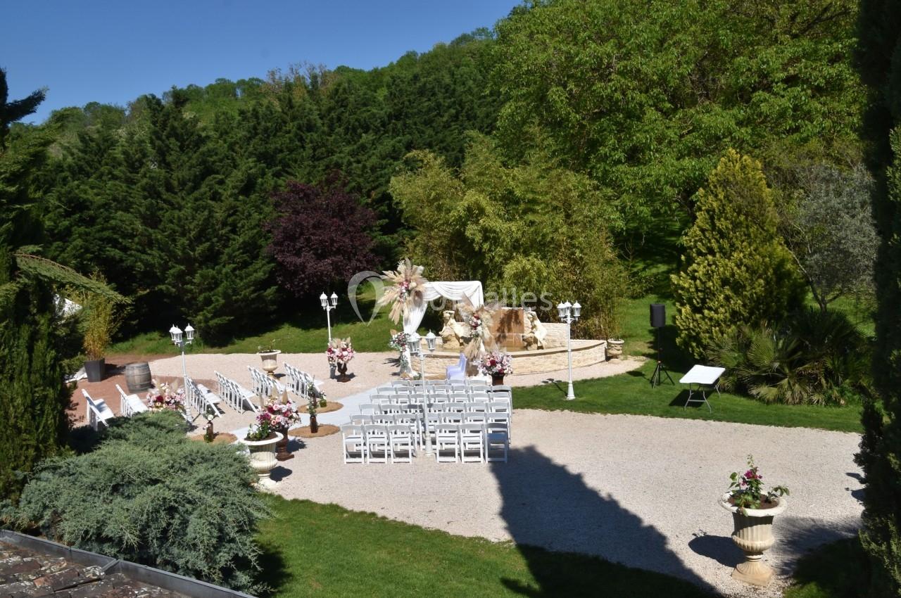 Chaises blanches alignées en extérieur pour une cérémonie, entourées de verdure et de décorations florales.