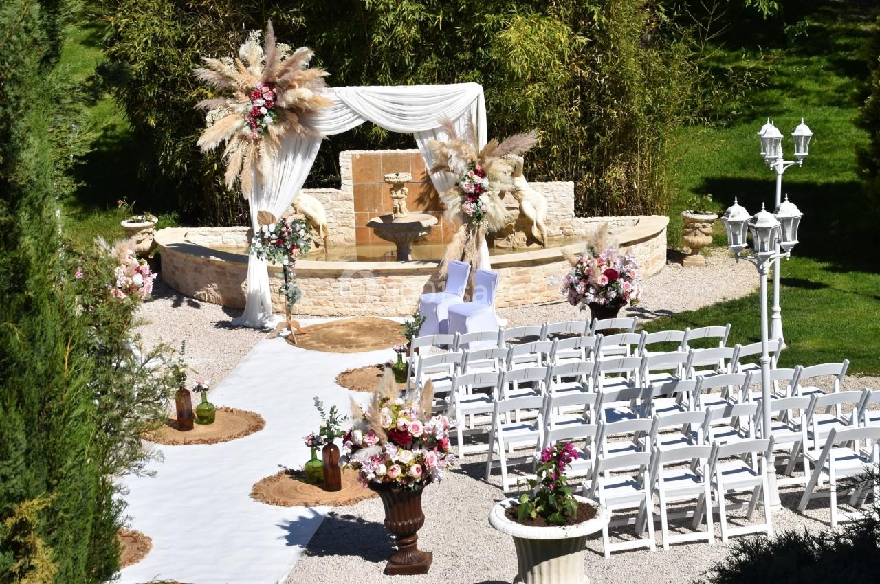 Allée centrale décorée menant à une arche de mariage ornée de fleurs et de voilages, entourée de chaises blanches.
