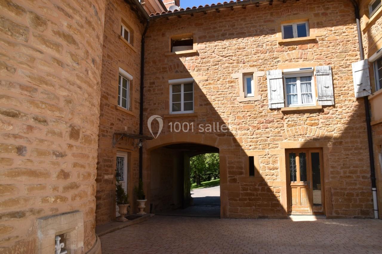 Cour intérieure en pierre dorée avec une arche menant à un espace ouvert, entourée de fenêtres et volets en bois.