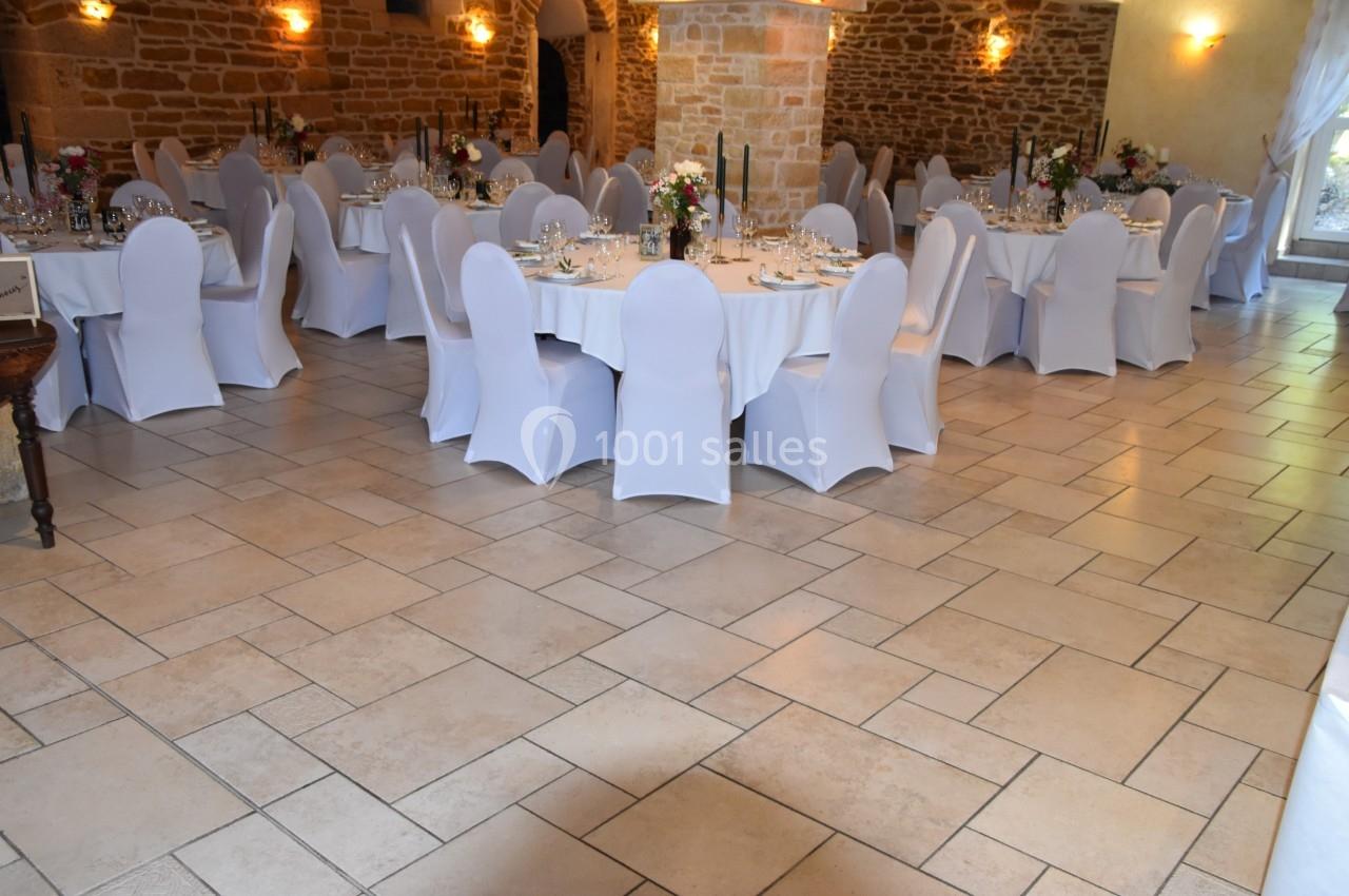 Salle de réception décorée avec des tables rondes dressées, nappes blanches et chaises houssées, éclairage chaleureux.