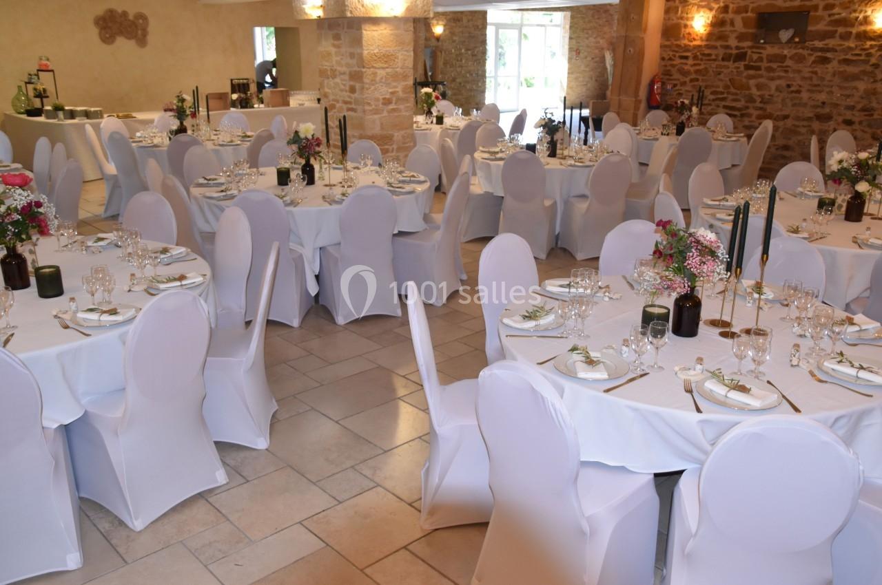 Salle de réception décorée avec des tables rondes dressées, nappes blanches, chaises houssées et arrangements floraux.