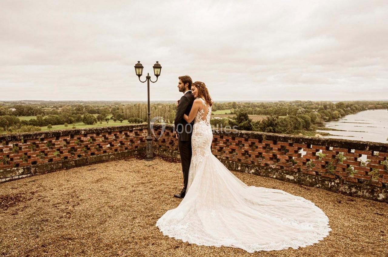 Un couple en tenue de mariage se tient sur une terrasse surplombant un paysage verdoyant et un cours d'eau.