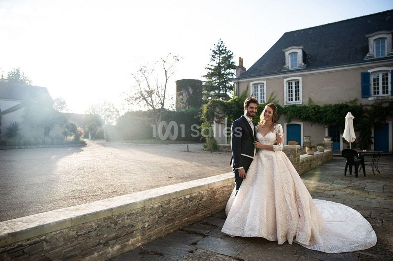 Un couple en tenue de mariage pose devant un bâtiment ancien avec des volets bleus, sous une lumière douce.