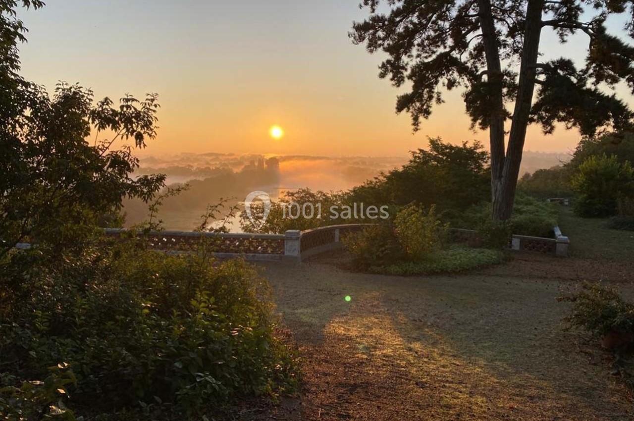Lever de soleil illuminant un jardin avec des arbres, un muret en pierre et une vue sur un paysage brumeux.