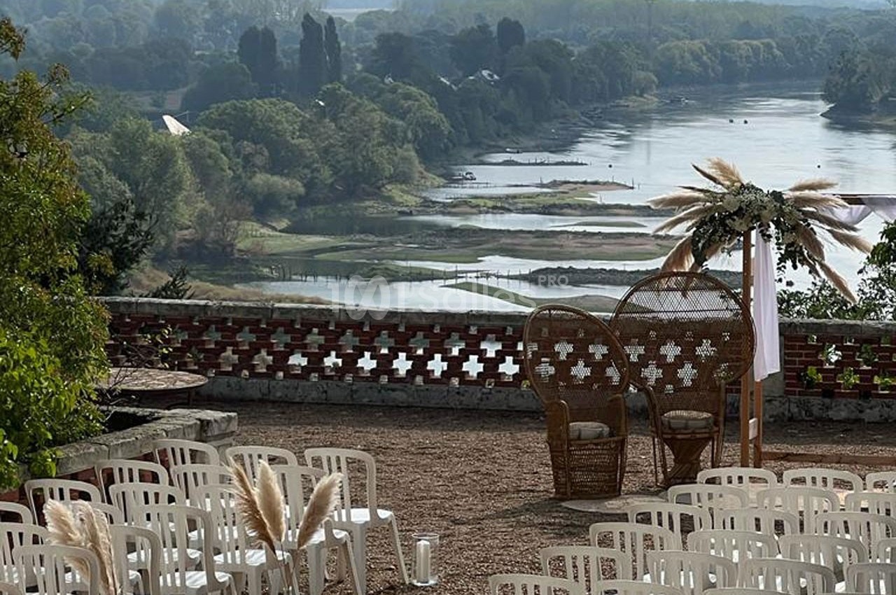 Vue d'un espace extérieur aménagé pour une cérémonie, avec des chaises blanches, des fauteuils en rotin et un paysage…