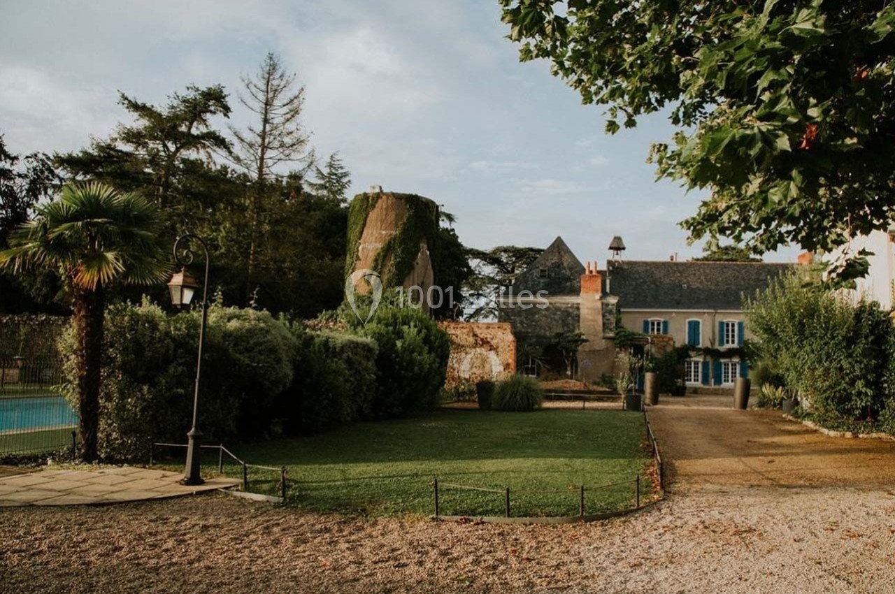 Jardin avec pelouse, arbres, piscine à gauche et bâtiment ancien en pierre avec volets bleus en arrière-plan.