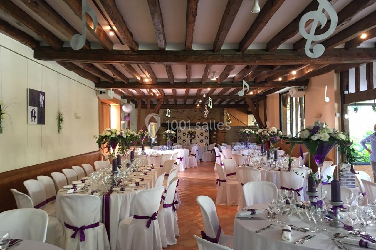 Location salle Saint-Léger-en-Bray (Oise) - Domaine du Colombier #10 Salle de réception décorée avec des tables dressées, des chaises blanches ornées de rubans violets et des notes de musique…