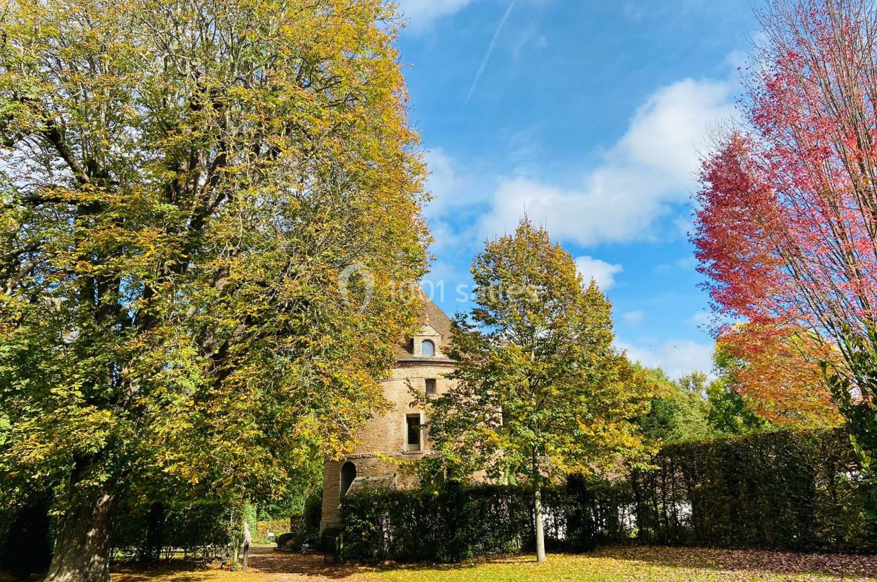 Location salle Saint-Léger-en-Bray (Oise) - Domaine du Colombier #14 Maison en pierre entourée d'arbres aux feuillages d'automne sous un ciel bleu partiellement nuageux.