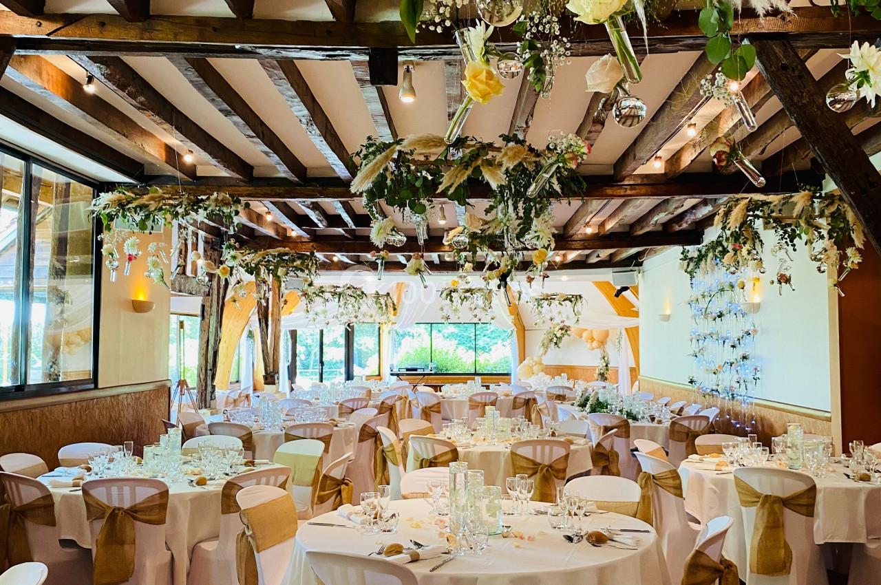 Location salle Saint-Léger-en-Bray (Oise) - Domaine du Colombier #17 Salle de réception décorée avec des tables rondes, nappes blanches et ornements floraux suspendus.