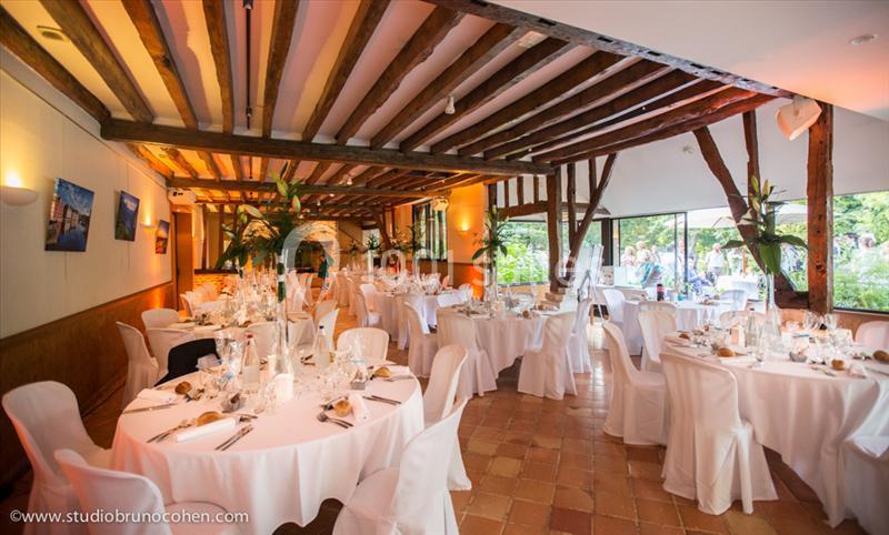 Location salle Saint-Léger-en-Bray (Oise) - Domaine du Colombier #2 Salle de réception lumineuse avec tables rondes décorées pour un événement, poutres apparentes et grandes baies vitrées.