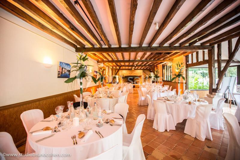 Location salle Saint-Léger-en-Bray (Oise) - Domaine du Colombier #3 Salle de réception lumineuse avec tables rondes dressées, chaises blanches et poutres apparentes au plafond.