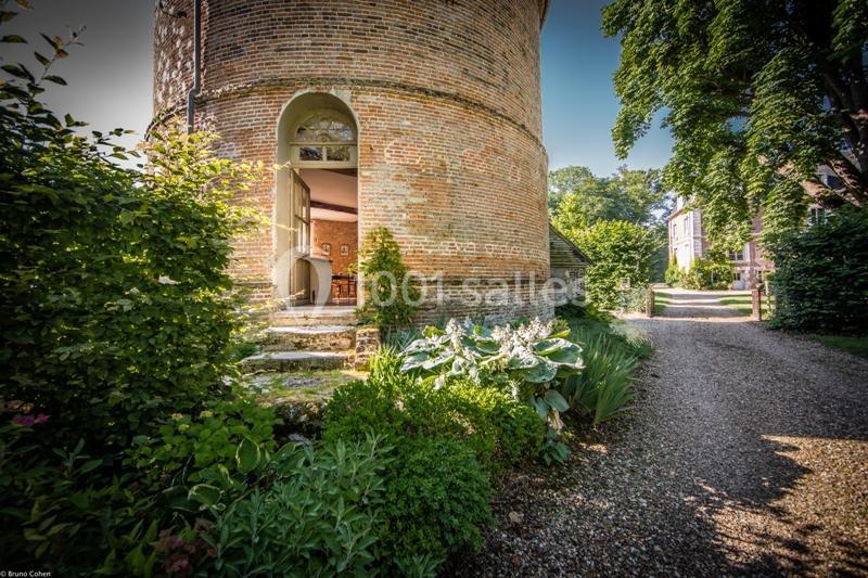 Location salle Saint-Léger-en-Bray (Oise) - Domaine du Colombier #8 Entrée d'un bâtiment en briques rond avec porte ouverte, entouré de verdure et d'un chemin de gravier.