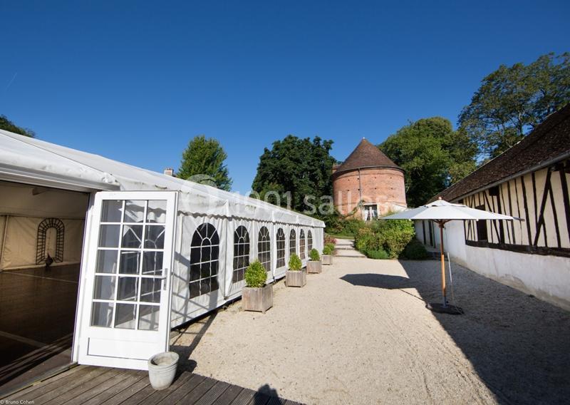 Location salle Saint-Léger-en-Bray (Oise) - Domaine du Colombier #6 Cour extérieure avec une tente blanche, un pigeonnier en briques, des arbres et des bâtiments à colombages.