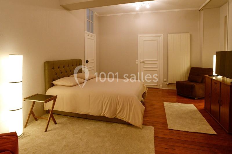 Chambre spacieuse avec lit double, parquet, éclairage doux, fauteuil, tapis et mobilier en bois clair.