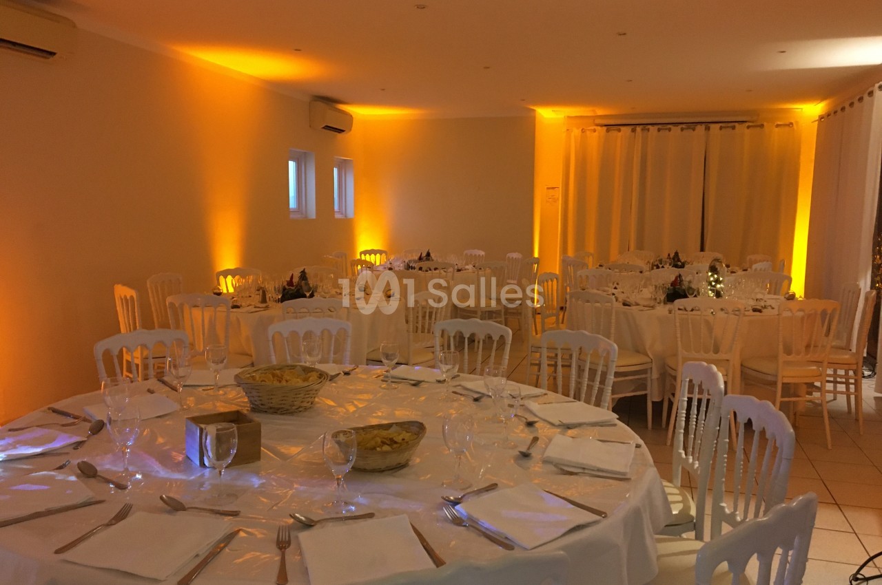 Salle de réception décorée avec des tables rondes dressées, éclairage chaleureux et ambiance élégante.