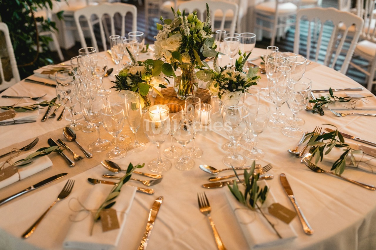 Table élégamment dressée avec vaisselle, couverts dorés, bougies et centre de table floral.