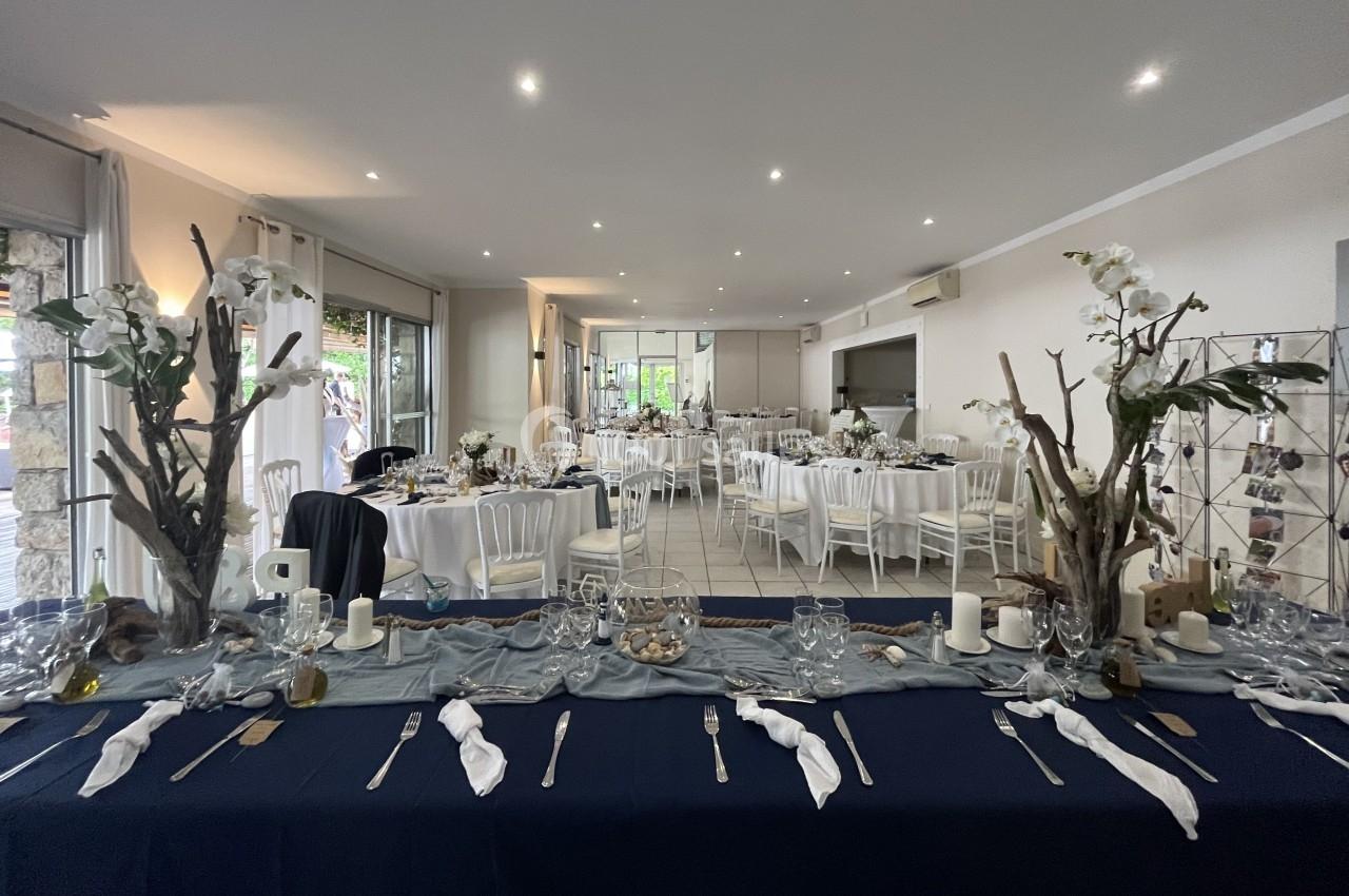 Salle de réception décorée avec des tables dressées, nappes blanches et bleues, et ornements floraux élégants.