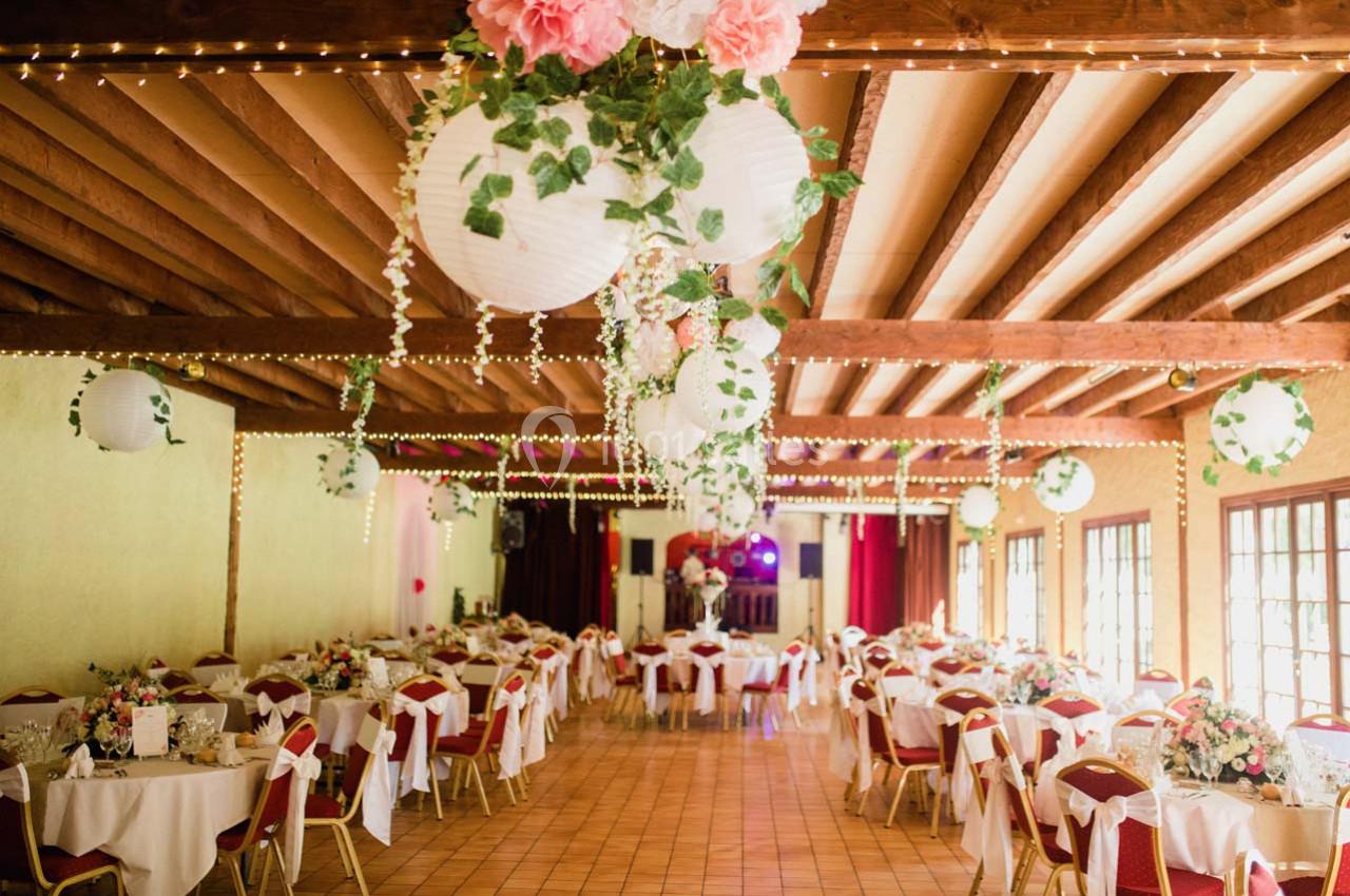 Salle de réception décorée avec des lanternes blanches, guirlandes lumineuses, tables dressées et chaises rouges.