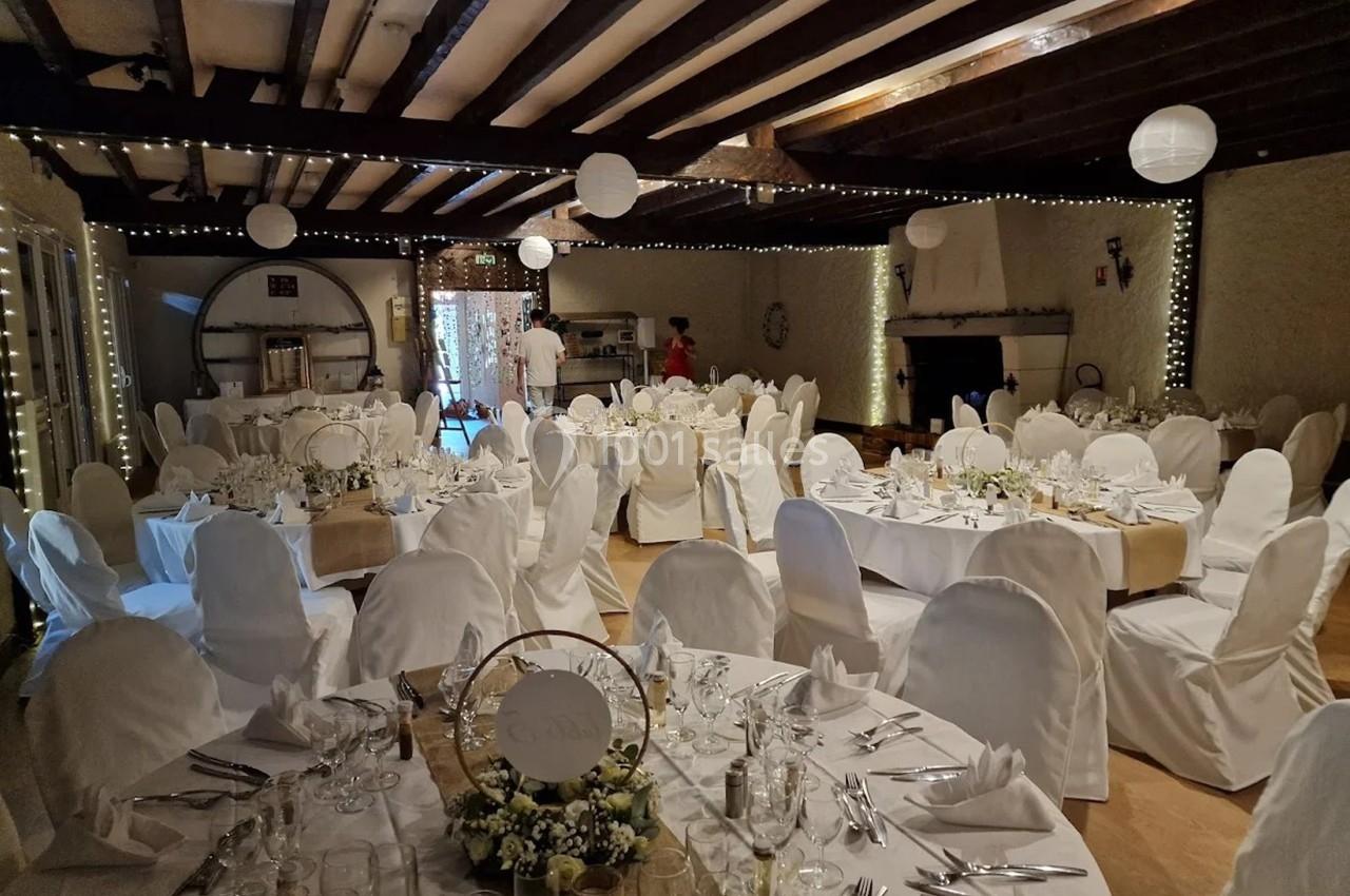 Salle de réception décorée avec des tables rondes dressées, nappes blanches et guirlandes lumineuses suspendues.