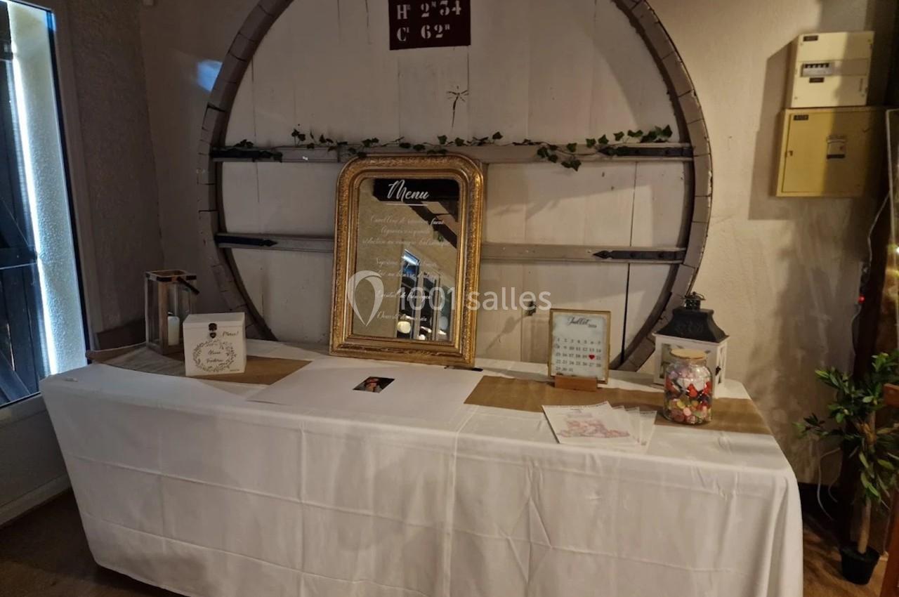 Table décorative avec nappe blanche, cadre doré affichant un menu, et divers éléments décoratifs dans un cadre rustique.