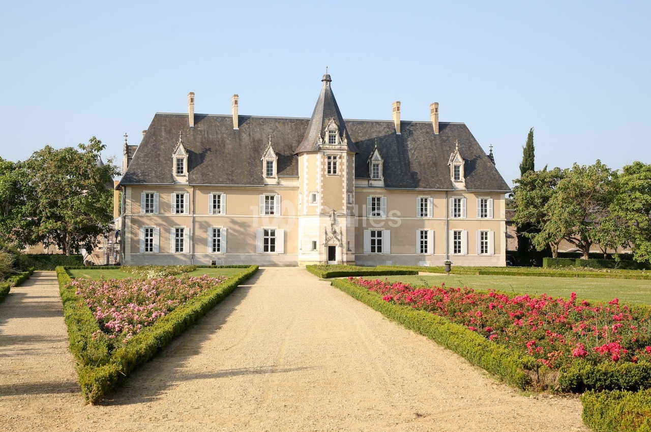 Façade d'un château historique entouré de jardins fleuris et d'une allée centrale en gravier.
