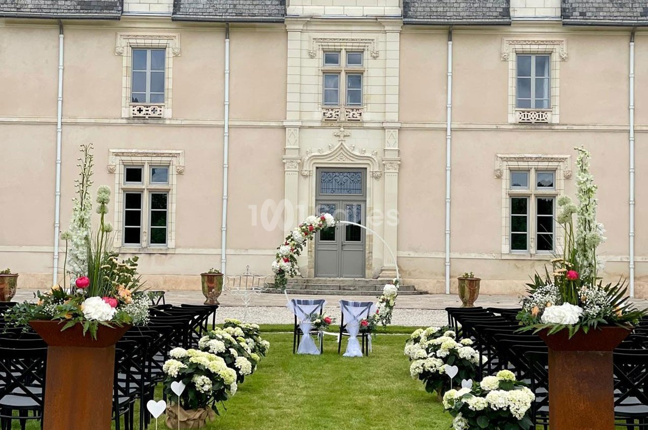 Cérémonie de mariage en plein air devant une façade de château, avec allée décorée de fleurs et arche florale.