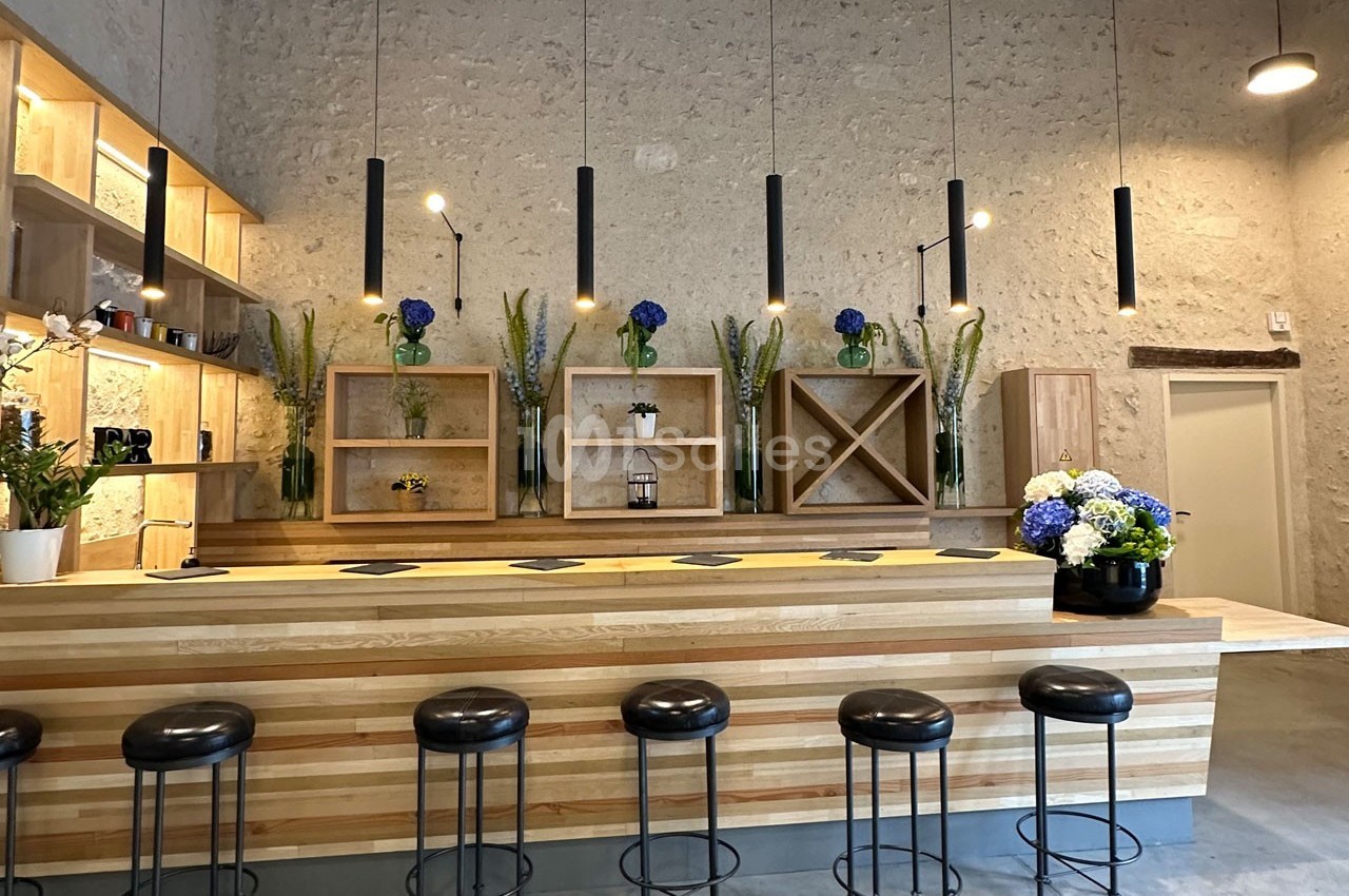 Un bar en bois clair avec des tabourets noirs, des étagères décorées de fleurs et un éclairage suspendu moderne.